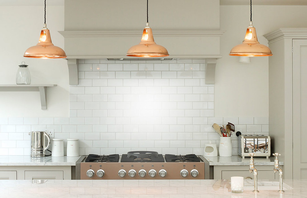 Klassisk inredning av ett kök, med en undermonterad diskho, grå skåp, vitt stänkskydd, stänkskydd i tunnelbanekakel, rostfria vitvaror och en köksö