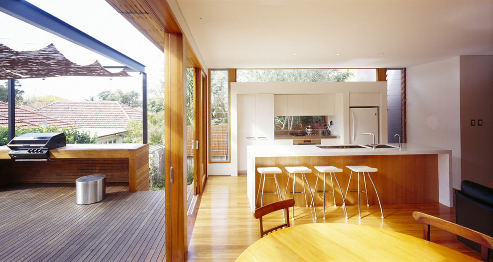 Offene, Zweizeilige, Mittelgroße Moderne Küchenbar mit flächenbündigen Schrankfronten, weißen Schränken, weißen Elektrogeräten, Unterbauwaschbecken, braunem Holzboden und Kücheninsel in Sydney