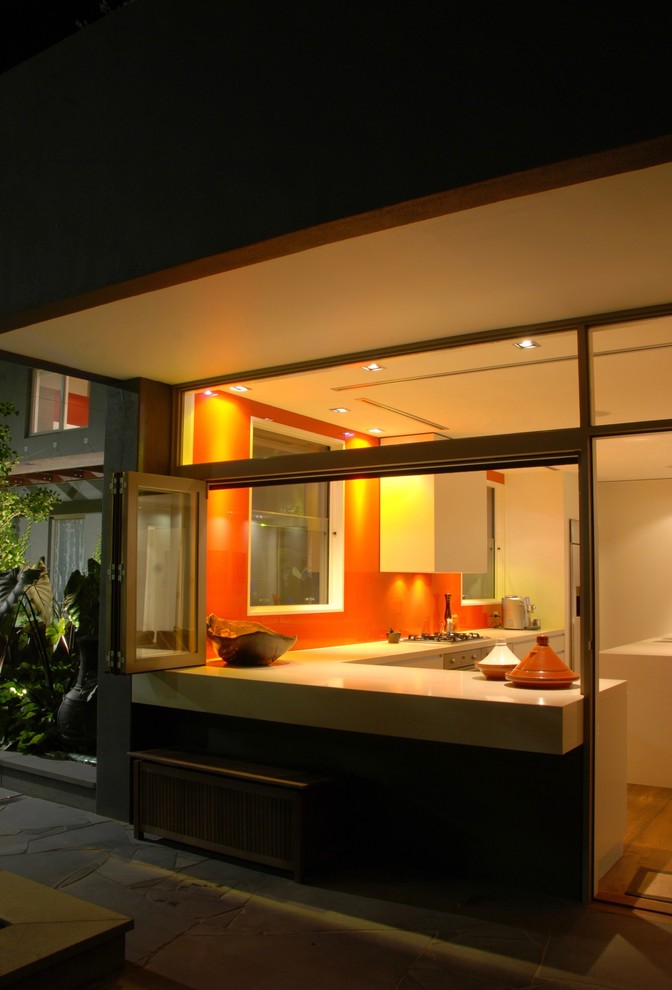 Idée de décoration pour une cuisine ouverte design en L avec un placard à porte plane, des portes de placard blanches, une crédence orange et îlot.