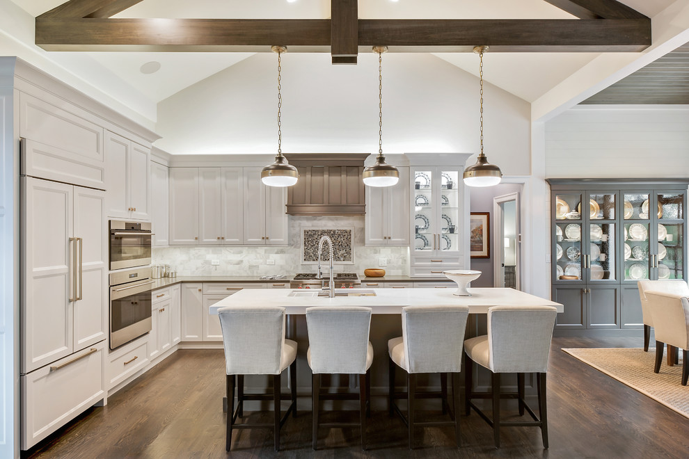 Large traditional l-shaped open plan kitchen in Chicago with a submerged sink, white cabinets, marble splashback, dark hardwood flooring, an island, brown floors, recessed-panel cabinets, white splashback and integrated appliances.