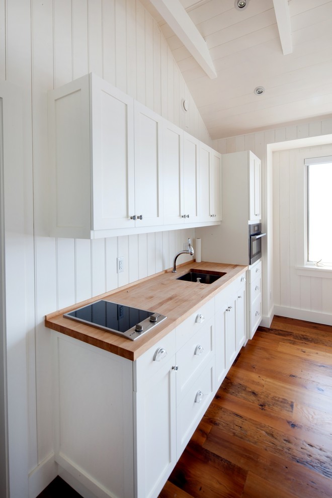 Ejemplo de cocina lineal clásica pequeña abierta con fregadero encastrado, salpicadero blanco, electrodomésticos de acero inoxidable y suelo marrón