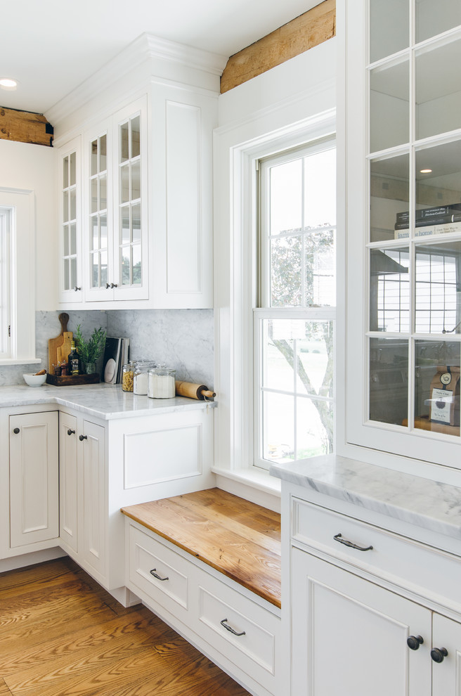 Example of a large country medium tone wood floor eat-in kitchen design in New York with a farmhouse sink, beaded inset cabinets, white cabinets, marble countertops, white backsplash, stone slab backsplash, stainless steel appliances and an island