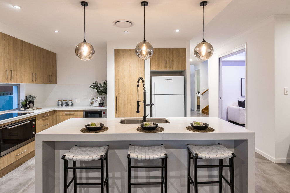 Moderne Küche in L-Form mit Doppelwaschbecken, flächenbündigen Schrankfronten, hellbraunen Holzschränken, Rückwand-Fenster, schwarzen Elektrogeräten, Kücheninsel, grauem Boden und weißer Arbeitsplatte in Brisbane