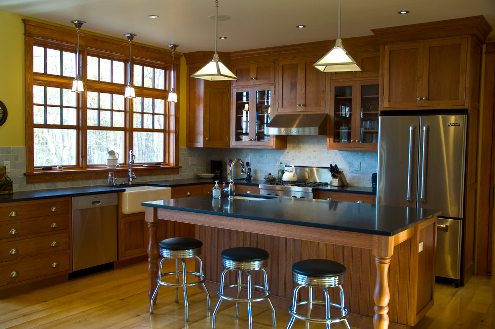 Klassisk inredning av ett mellanstort kök, med en rustik diskho, skåp i shakerstil, skåp i mellenmörkt trä, granitbänkskiva, grått stänkskydd, stänkskydd i keramik, rostfria vitvaror, ljust trägolv och en köksö