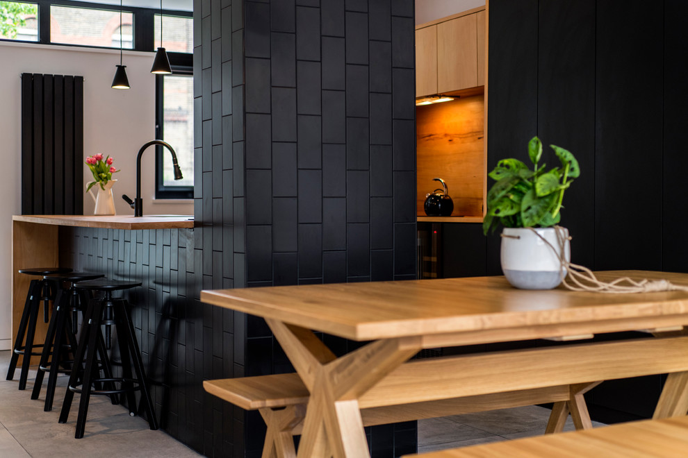 Offene, Zweizeilige, Kleine Moderne Küche mit flächenbündigen Schrankfronten, schwarzen Schränken, Arbeitsplatte aus Holz, schwarzen Elektrogeräten, Porzellan-Bodenfliesen und Kücheninsel in London