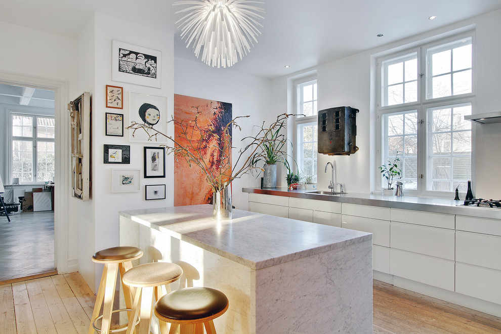This is an example of a large contemporary galley kitchen/diner in Copenhagen with flat-panel cabinets, white cabinets, medium hardwood flooring, an island, a built-in sink, marble worktops, white splashback and white appliances.