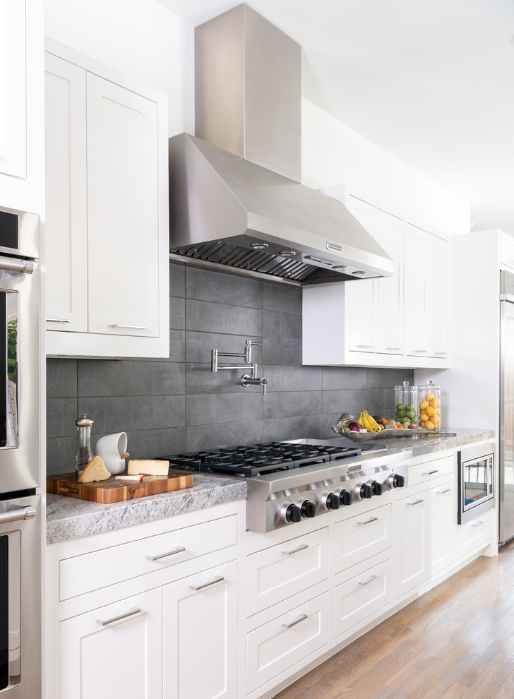 Klassisk inredning av ett grå grått kök, med skåp i shakerstil, vita skåp, grått stänkskydd, rostfria vitvaror, mellanmörkt trägolv och brunt golv