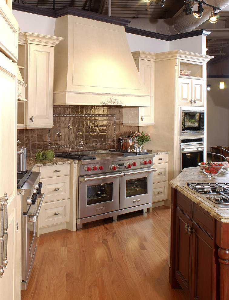 Example of a mid-sized classic l-shaped medium tone wood floor enclosed kitchen design in Boston with raised-panel cabinets, beige cabinets, granite countertops, metallic backsplash, metal backsplash, stainless steel appliances, an undermount sink and an island