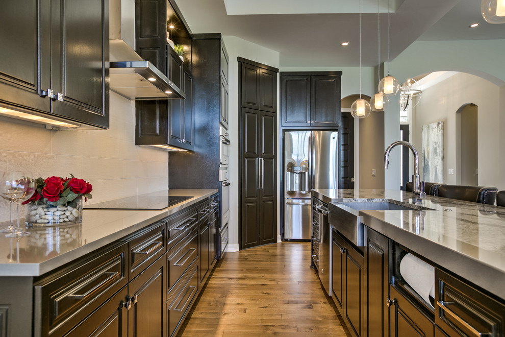 オマハにあるコンテンポラリースタイルのおしゃれなアイランドキッチン (レイズドパネル扉のキャビネット、濃色木目調キャビネット、シルバーの調理設備、淡色無垢フローリング) の写真