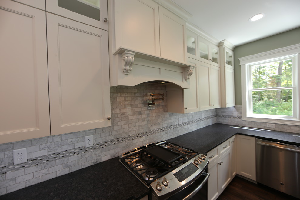 Exempel på ett mellanstort amerikanskt kök, med en rustik diskho, släta luckor, vita skåp, granitbänkskiva, grått stänkskydd, stänkskydd i travertin, rostfria vitvaror, mellanmörkt trägolv, en köksö och brunt golv