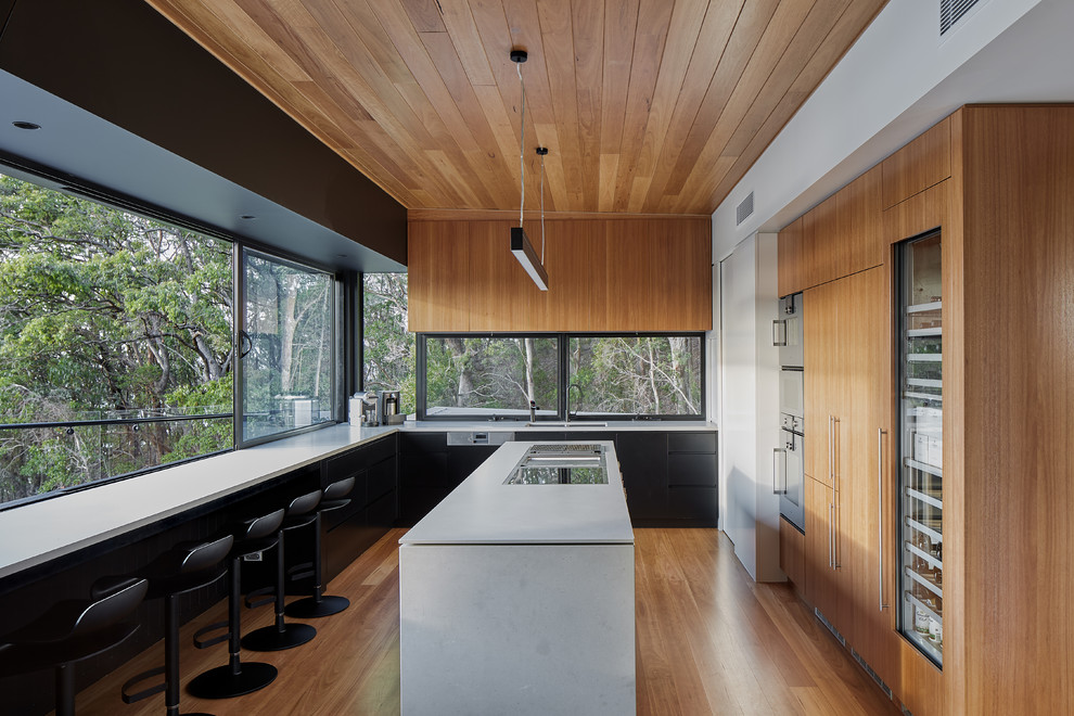 Immagine di una cucina design con ante lisce, ante in legno scuro, elettrodomestici in acciaio inossidabile, pavimento in legno massello medio, pavimento marrone e top bianco