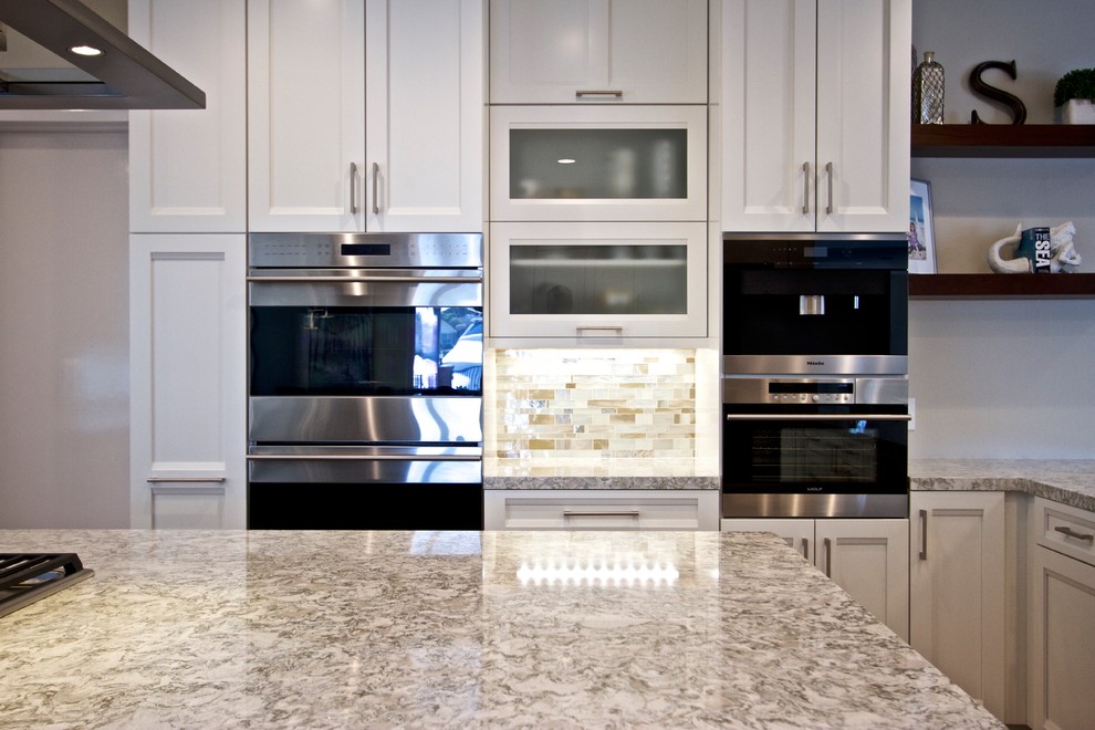 Klassisk inredning av ett kök, med en undermonterad diskho, luckor med infälld panel, vita skåp, stänkskydd i mosaik, rostfria vitvaror, mellanmörkt trägolv, en köksö och brunt golv