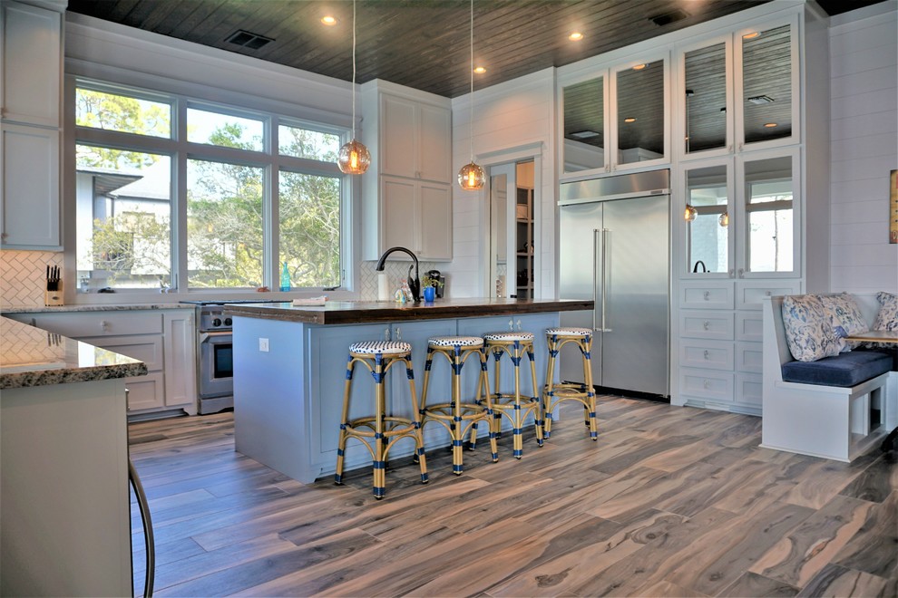 Geräumige Küche in U-Form mit weißen Schränken, Granit-Arbeitsplatte, Küchengeräten aus Edelstahl, hellem Holzboden und Kücheninsel in Sonstige