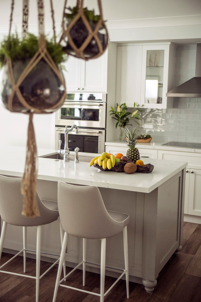 Skandinavisk inredning av ett mellanstort kök, med en köksö, en undermonterad diskho, skåp i shakerstil, vita skåp, bänkskiva i kvarts, vitt stänkskydd, stänkskydd i glaskakel, rostfria vitvaror, klinkergolv i porslin och brunt golv