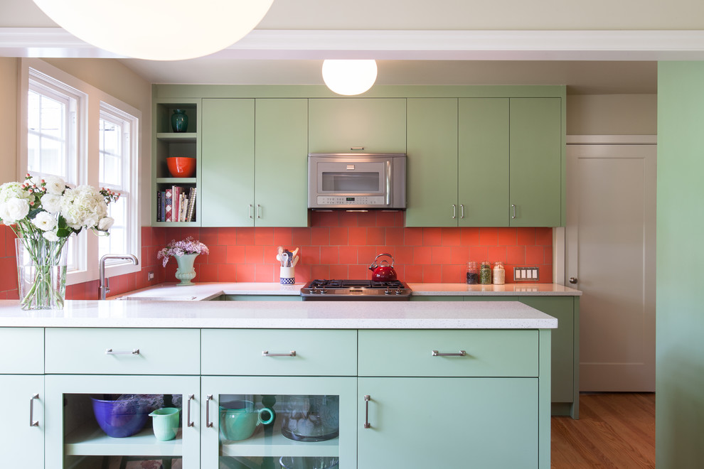 Klassisk inredning av ett litet kök, med en undermonterad diskho, släta luckor, gröna skåp, bänkskiva i återvunnet glas, orange stänkskydd, stänkskydd i keramik, rostfria vitvaror och ljust trägolv