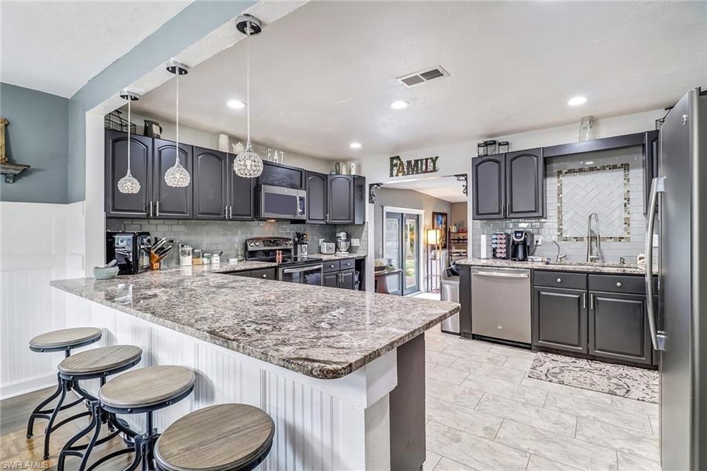 Inspiration for a mid-sized transitional u-shaped porcelain tile and gray floor eat-in kitchen remodel in Miami with an undermount sink, raised-panel cabinets, gray cabinets, granite countertops, gray backsplash, glass tile backsplash, stainless steel appliances, a peninsula and multicolored countertops