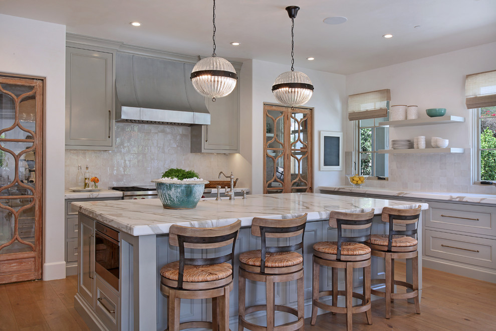 Klassische Küche in L-Form mit Kassettenfronten, grauen Schränken, Küchenrückwand in Weiß, Küchengeräten aus Edelstahl, braunem Holzboden, Kücheninsel und braunem Boden in Los Angeles