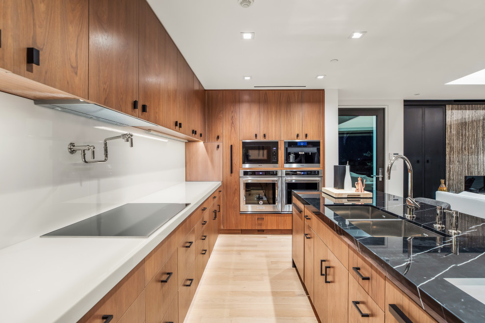 Foto di una cucina design con lavello sottopiano, ante lisce, ante in legno scuro, elettrodomestici in acciaio inossidabile, parquet chiaro, pavimento beige e top bianco