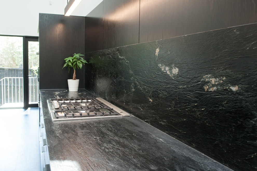 Inspiration for a medium sized modern galley kitchen/diner in Houston with a submerged sink, flat-panel cabinets, black cabinets, soapstone worktops, black splashback, stone slab splashback, integrated appliances, dark hardwood flooring, multiple islands, black floors and black worktops.