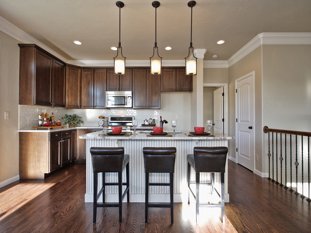 Transitional l-shaped medium tone wood floor and brown floor kitchen photo in Denver with an undermount sink, recessed-panel cabinets, granite countertops, white backsplash, subway tile backsplash, stainless steel appliances, medium tone wood cabinets and an island