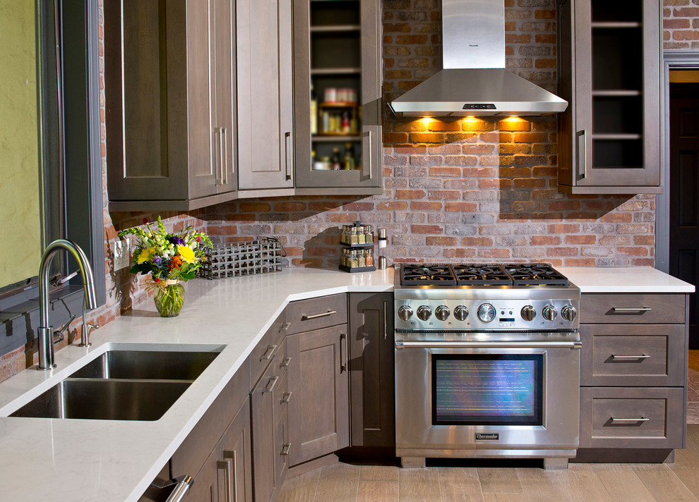 Bild på ett mellanstort funkis kök, med en undermonterad diskho, luckor med infälld panel, grå skåp, bänkskiva i kvarts, rött stänkskydd, rostfria vitvaror, ljust trägolv, stänkskydd i tegel och beiget golv