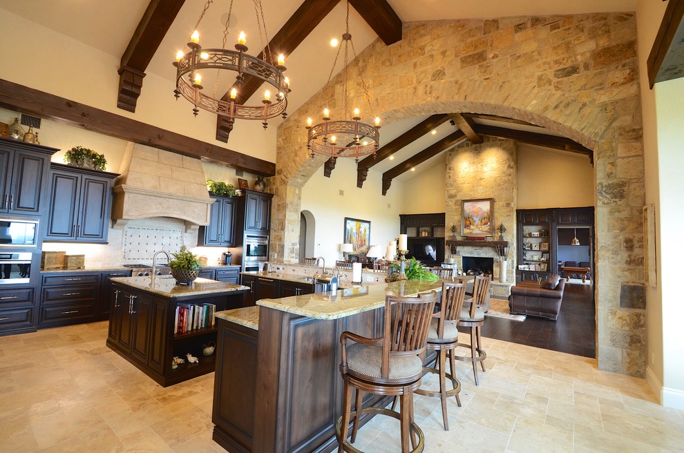 Large tuscan l-shaped travertine floor eat-in kitchen photo in Austin with an island, raised-panel cabinets, dark wood cabinets, granite countertops, beige backsplash, stainless steel appliances and porcelain backsplash