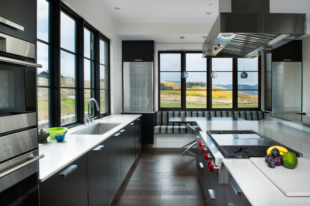 Immagine di una grande cucina design con lavello sottopiano, ante lisce, ante nere, elettrodomestici in acciaio inossidabile, parquet scuro, top in quarzo composito, pavimento marrone e top bianco