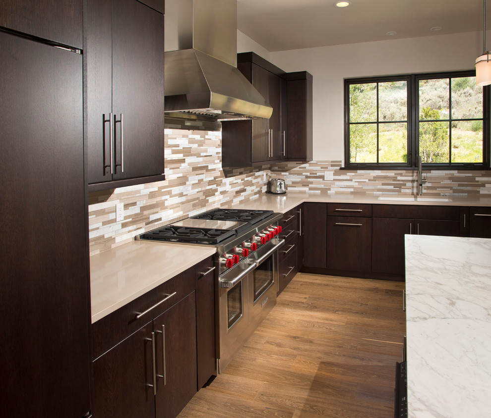 Ejemplo de cocina minimalista de tamaño medio con fregadero bajoencimera, armarios con paneles lisos, puertas de armario de madera en tonos medios, encimera de granito, salpicadero beige, salpicadero de azulejos de piedra, electrodomésticos con paneles, suelo de madera clara, una isla y suelo beige