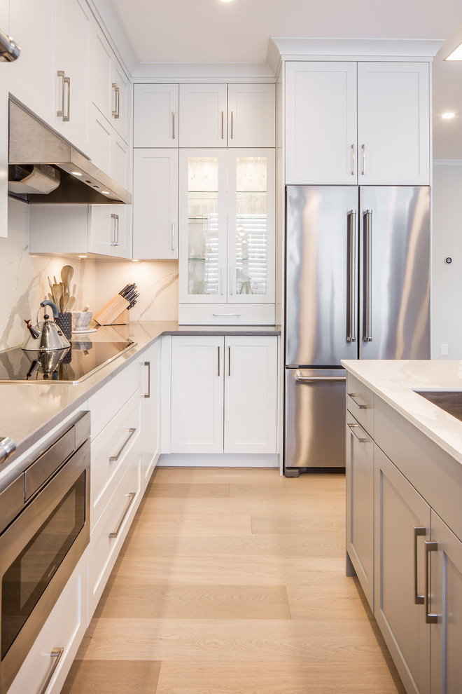 Inspiration for a small transitional l-shaped light wood floor and beige floor open concept kitchen remodel in Vancouver with an undermount sink, shaker cabinets, white cabinets, quartz countertops, white backsplash, porcelain backsplash, stainless steel appliances, an island and gray countertops