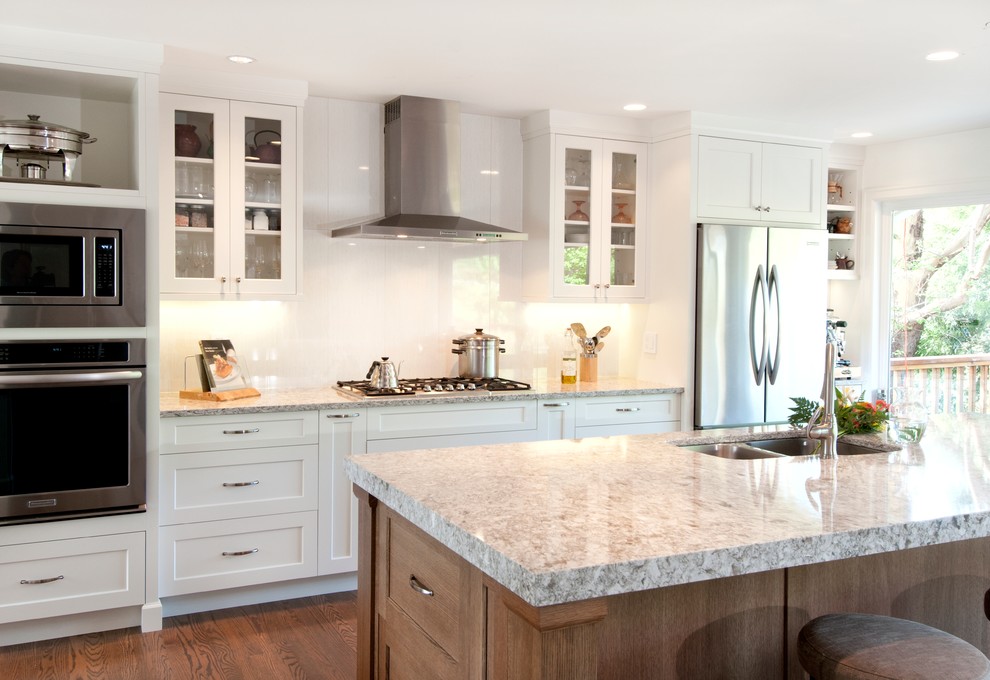 Photo of a medium sized classic kitchen/diner in Vancouver with a submerged sink, shaker cabinets, white cabinets, quartz worktops, white splashback, porcelain splashback, stainless steel appliances, medium hardwood flooring and an island.