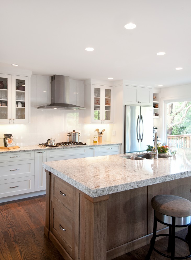 Design ideas for a medium sized traditional kitchen/diner in Vancouver with a submerged sink, shaker cabinets, white cabinets, quartz worktops, white splashback, porcelain splashback, stainless steel appliances, medium hardwood flooring and an island.
