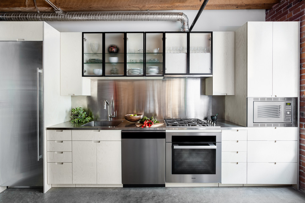 Idéer för att renovera ett litet industriellt linjärt kök och matrum, med en integrerad diskho, släta luckor, skåp i ljust trä, bänkskiva i rostfritt stål, rostfria vitvaror, betonggolv och grått golv