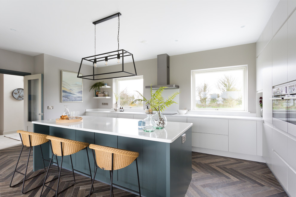 Inspiration for a large contemporary l-shaped kitchen/diner in Cork with a submerged sink, flat-panel cabinets, grey cabinets, quartz worktops, white splashback, glass sheet splashback, stainless steel appliances, ceramic flooring, an island, brown floors and white worktops.
