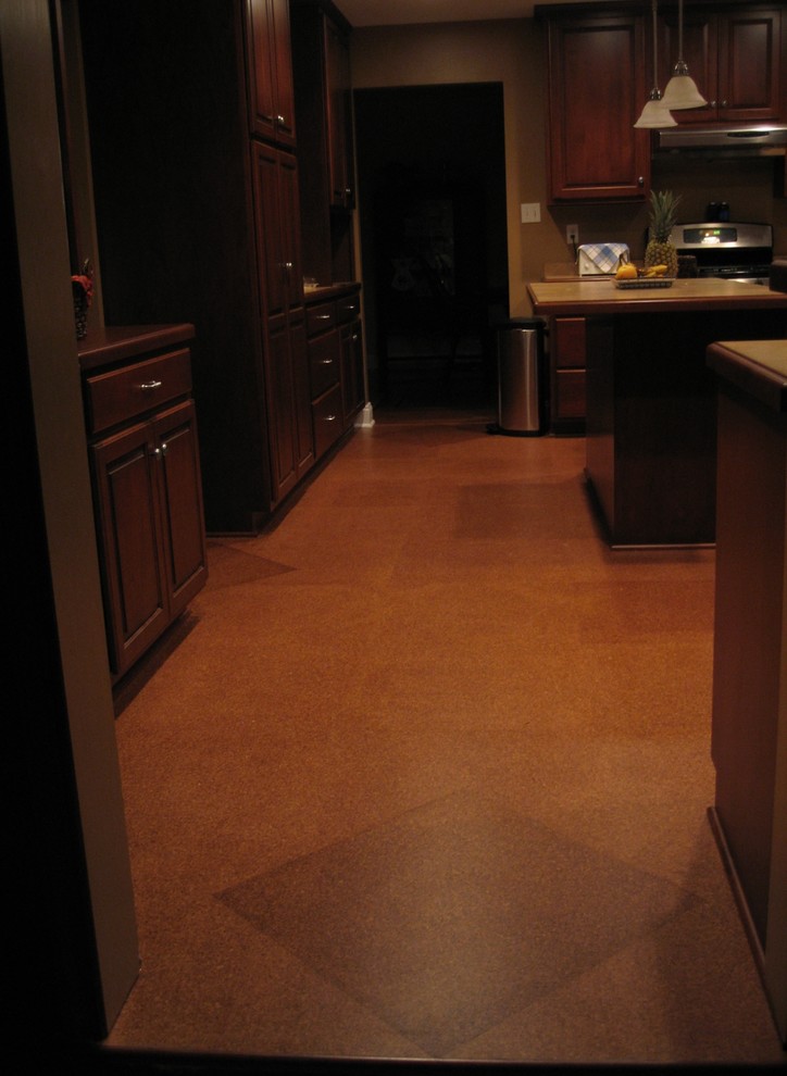 Immagine di una cucina chiusa e di medie dimensioni con pavimento in sughero, ante con bugna sagomata, ante in legno bruno e elettrodomestici in acciaio inossidabile