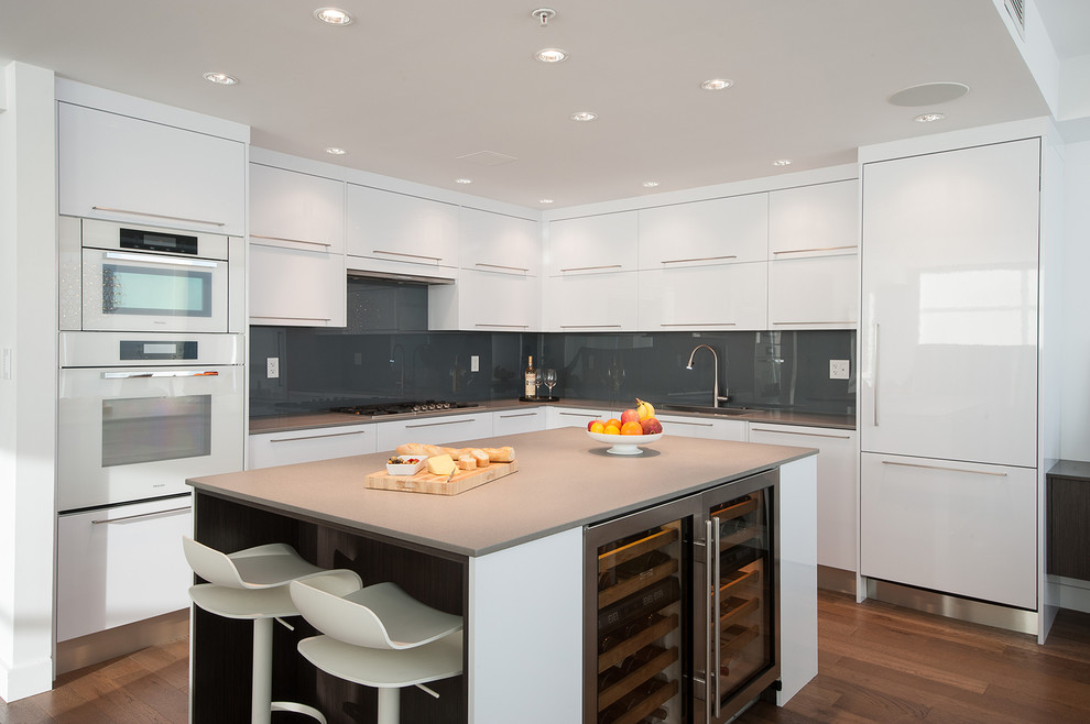 Moderne Küche in L-Form mit flächenbündigen Schrankfronten, weißen Schränken, Küchenrückwand in Grau, Glasrückwand, weißen Elektrogeräten, dunklem Holzboden, Kücheninsel, braunem Boden und grauer Arbeitsplatte in Vancouver