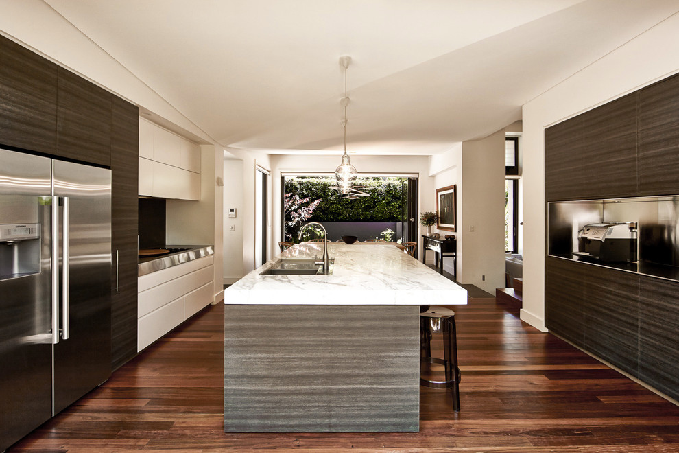 Bild på ett funkis kök, med stänkskydd med metallisk yta, rostfria vitvaror, mellanmörkt trägolv, brunt golv, vita skåp, marmorbänkskiva och en köksö