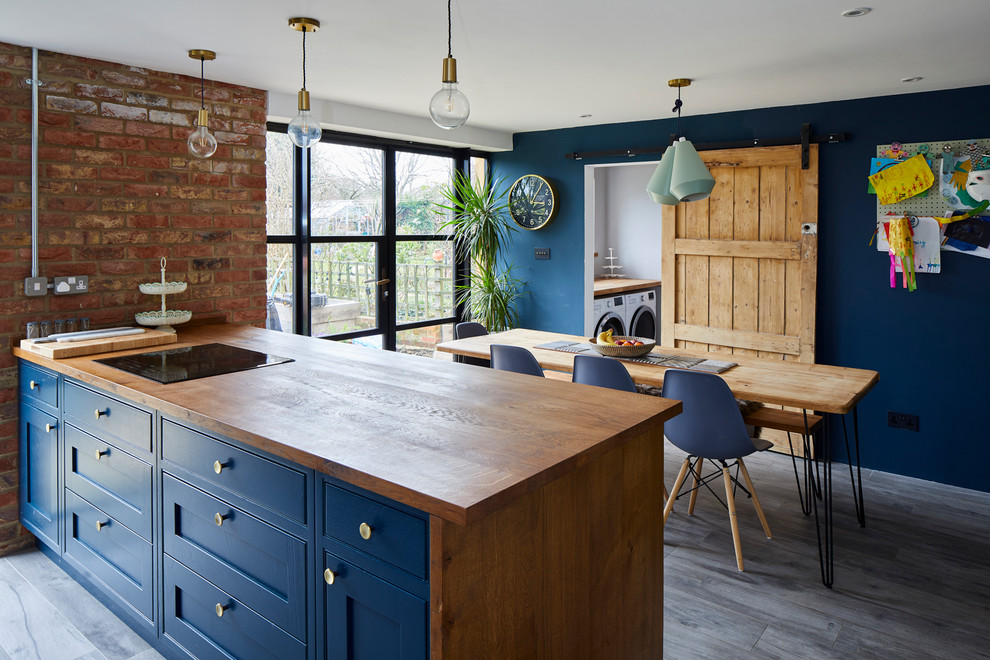 Design ideas for a contemporary galley kitchen/diner in London with a submerged sink, shaker cabinets, blue cabinets, wood worktops, stainless steel appliances, a breakfast bar, grey floors and brown worktops.