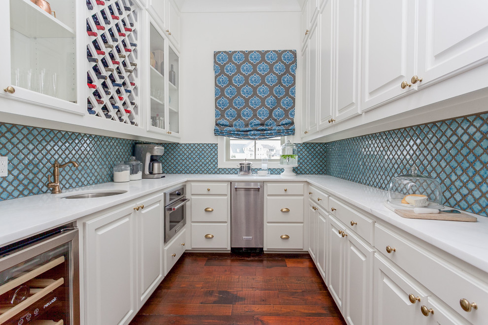 Transitional u-shaped medium tone wood floor kitchen photo in New Orleans with an undermount sink, raised-panel cabinets, white cabinets, blue backsplash, stainless steel appliances and no island