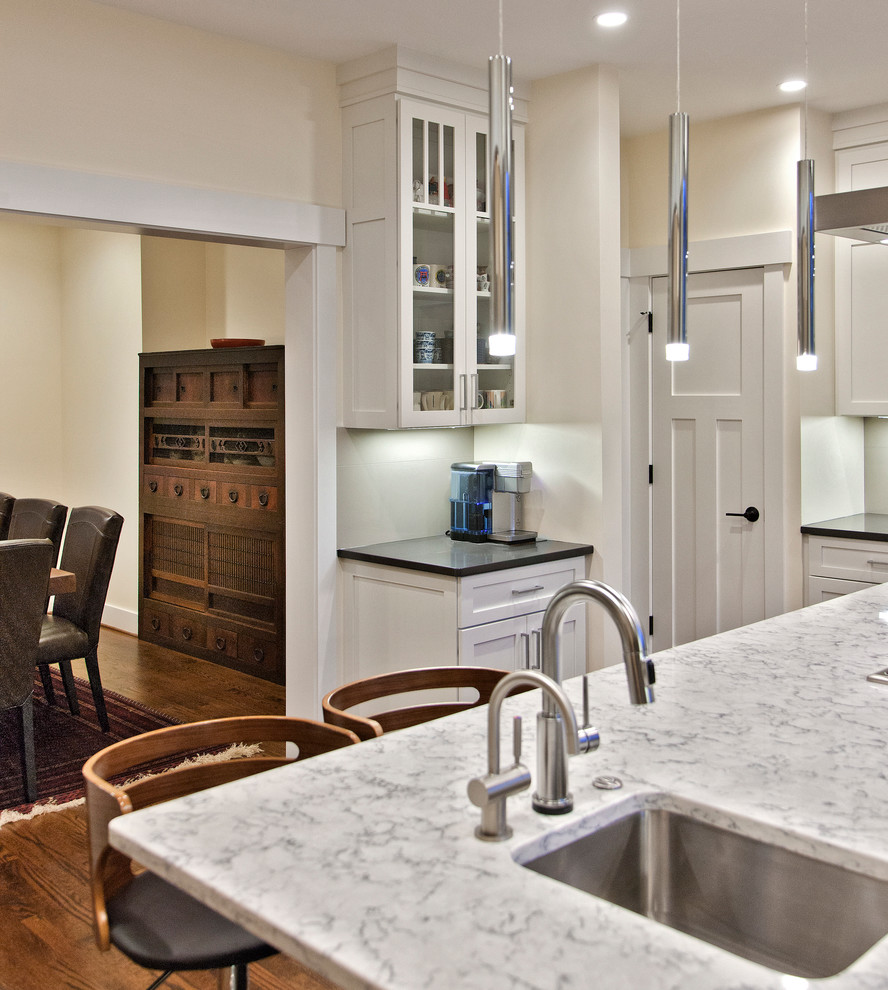 Inspiration for a medium sized world-inspired l-shaped kitchen in DC Metro with a submerged sink, shaker cabinets, white cabinets, composite countertops, stainless steel appliances, dark hardwood flooring, an island, brown floors and black worktops.