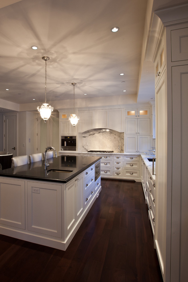 Eat-in kitchen - huge traditional l-shaped dark wood floor eat-in kitchen idea in Vancouver with an undermount sink, recessed-panel cabinets, white cabinets, quartz countertops, gray backsplash, stone slab backsplash, stainless steel appliances and an island