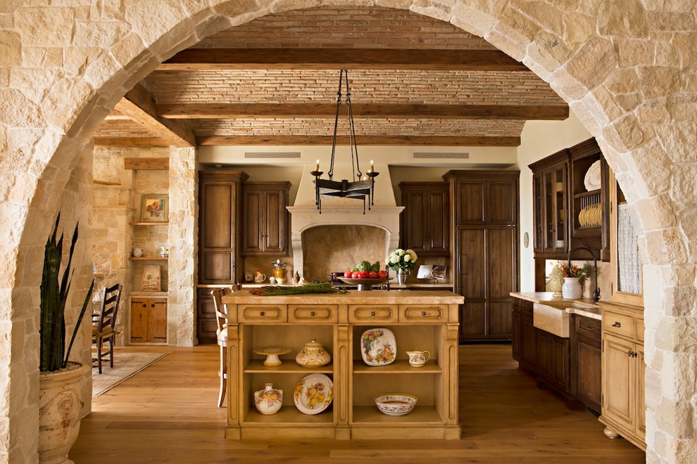 Foto di un cucina con isola centrale mediterraneo con lavello stile country, ante in legno bruno, paraspruzzi beige e pavimento in legno massello medio