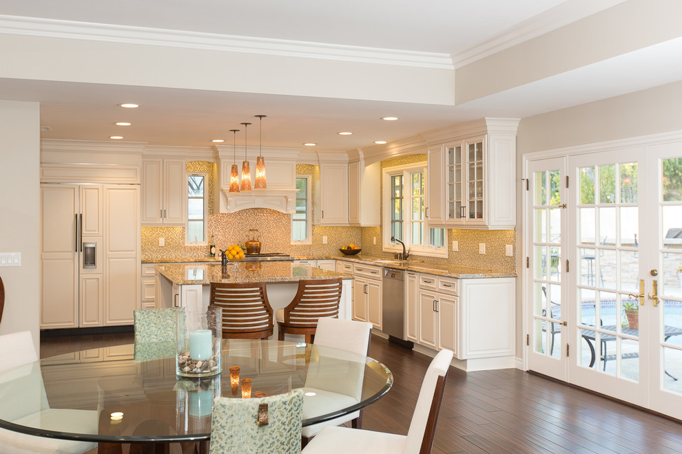 Open concept kitchen - large traditional u-shaped medium tone wood floor open concept kitchen idea in Orange County with a double-bowl sink, raised-panel cabinets, white cabinets, granite countertops, multicolored backsplash, glass tile backsplash, stainless steel appliances and an island