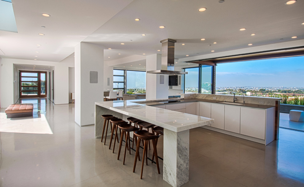 Example of a large trendy u-shaped concrete floor and brown floor open concept kitchen design in Orange County with an undermount sink, flat-panel cabinets, white cabinets, a peninsula, marble countertops and stainless steel appliances