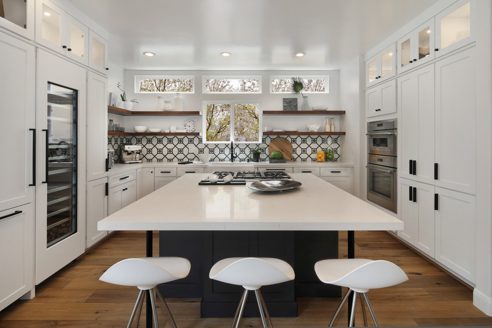 Bild på ett mellanstort funkis vit vitt u-kök, med en rustik diskho, skåp i shakerstil, vita skåp, bänkskiva i kvarts, flerfärgad stänkskydd, stänkskydd i cementkakel, integrerade vitvaror, mellanmörkt trägolv, en köksö och brunt golv