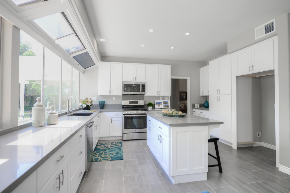Photo of a medium sized traditional l-shaped kitchen/diner in Los Angeles with a double-bowl sink, shaker cabinets, white cabinets, composite countertops, stainless steel appliances, cement flooring and an island.