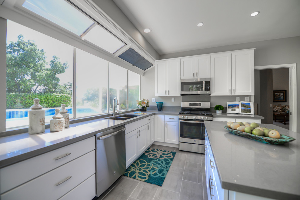 Design ideas for a medium sized classic l-shaped kitchen/diner in Los Angeles with a double-bowl sink, shaker cabinets, white cabinets, composite countertops, stainless steel appliances, cement flooring and an island.