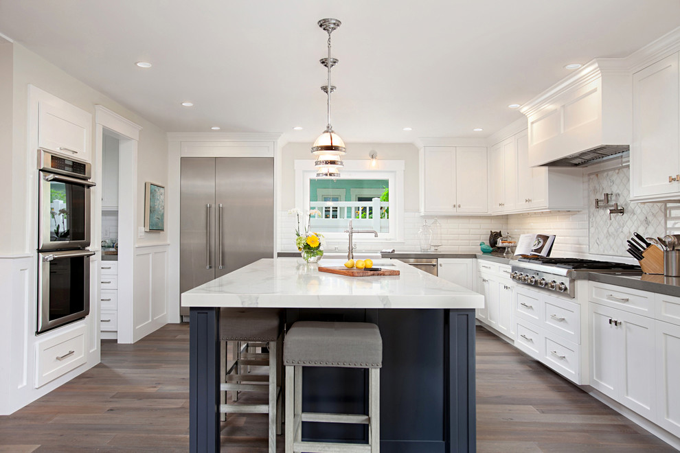 Inspiration for a classic l-shaped kitchen in San Diego with a belfast sink, shaker cabinets, white cabinets, white splashback, metro tiled splashback, stainless steel appliances, dark hardwood flooring and an island.