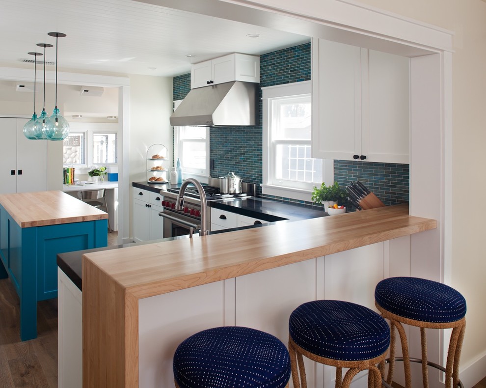 This is an example of a coastal l-shaped kitchen in San Diego with shaker cabinets, white cabinets, blue splashback, mosaic tiled splashback, stainless steel appliances, medium hardwood flooring and an island.