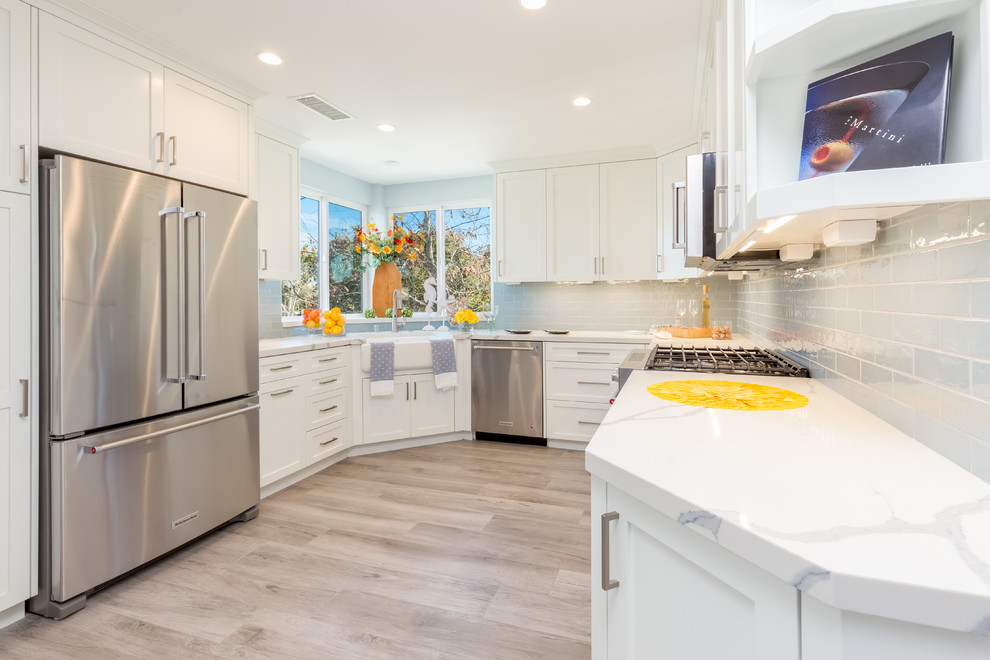 Photo of a coastal u-shaped kitchen in San Diego with a belfast sink, shaker cabinets, stainless steel cabinets, engineered stone countertops, blue splashback, ceramic splashback, stainless steel appliances, porcelain flooring and grey floors.