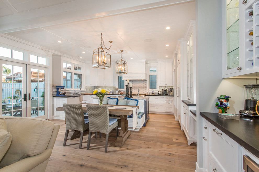 Inspiration for a mid-sized timeless u-shaped light wood floor and beige floor open concept kitchen remodel in San Diego with an undermount sink, shaker cabinets, white cabinets, granite countertops, beige backsplash, porcelain backsplash, stainless steel appliances and an island